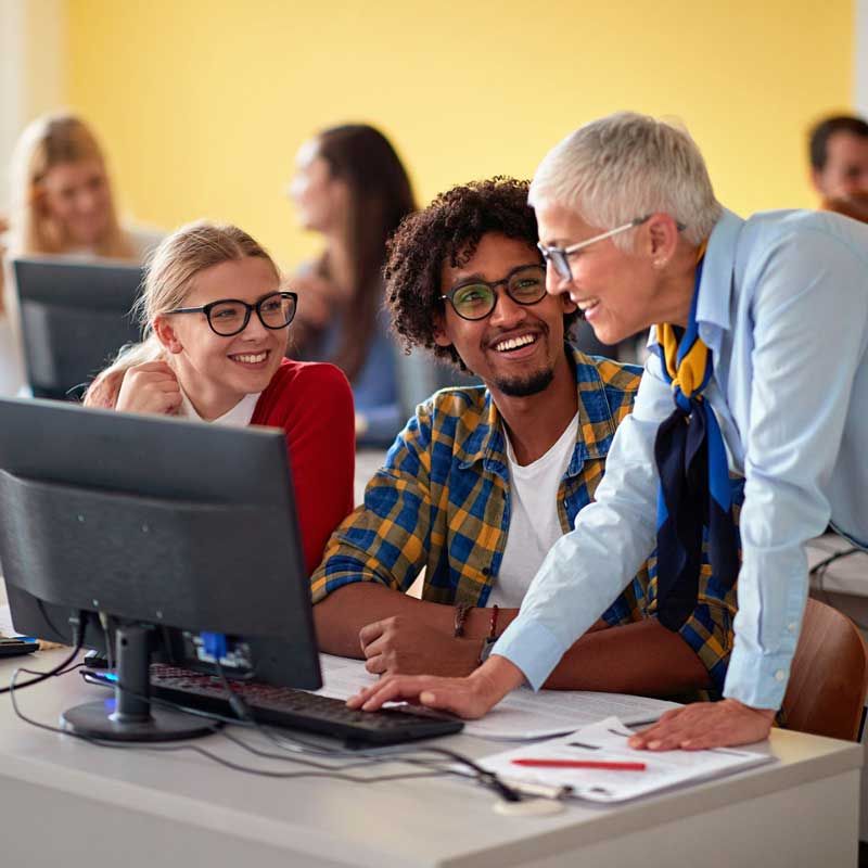 Happy teacher and students working at a computer.